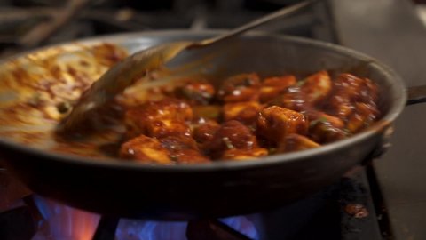 Chef tosses traditional paneer tikka masala over flame, close up slow motion 4K