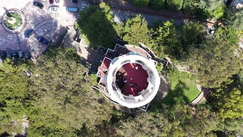 COIT Tower, Telegraph hill in San Francisco, CA. Drone shot looking straight down into the observation area of the tower with a slow pull back showing the parking area, cars, trees and people.