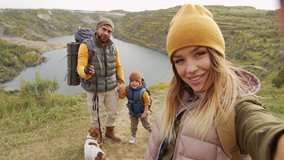 POV shot of happy young woman holding camera and taking selfie or filming herself and her cheerful husband, 5-year-old son and cute Jack Russell Terrier dog while hiking near quarry lake - Powered by Shutterstock - Get 15% off with code: PIKWIZARD15