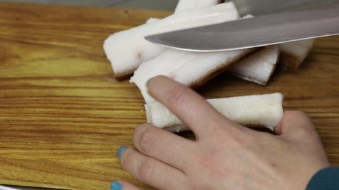 Cook cuts the skin off the lard with a knife.