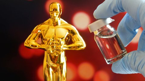 Hollywood Golden Oscar Academy award statue and hand in gloves with vaccine aganist coronavirus on blue background. Success and victory concept. Oscar ceremony in coronavirus time concept