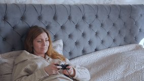 Woman playing computer games on bed with gamepad