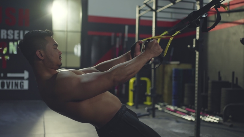 Asian active athlete man straight out his arms to hold TRX anchored to a steel beam in stadium, Lifting yourself up and down to maintaining muscle, build strength, flexibility at fitness club or gym. Royalty-Free Stock Footage #1069519903