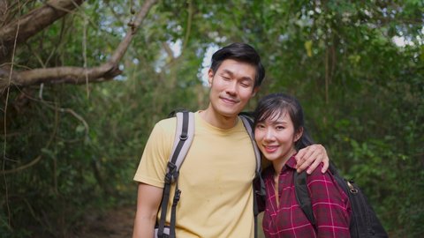 Portrait of Young Asian man and woman couple travel in the forest together for honeymoon or holiday trip. Friend feeling fresh and relax in nature wild, smiling look at camera with happiness and fun.