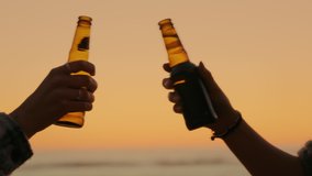 Close up of two friends enjoy drink of cold beer at beach sunset. Campfire party or beach bar vibes. Silhouette of two beer bottles chin and cheer, toast to summer vacation or holiday - Powered by Shutterstock - Get 15% off with code: PIKWIZARD15