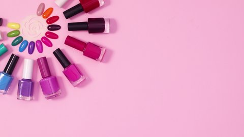 6k Nail polish bottles appear around nail color samples on pastel pink background. Stop motion flat lay