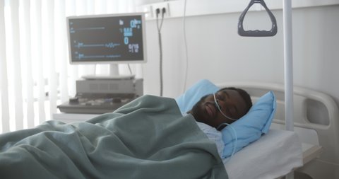 Portrait of afro-american man in coma dying in hospital bed with heart rate falling on ecg monitor. African sick male patient in intensive care unit dead with no heart rate on screen