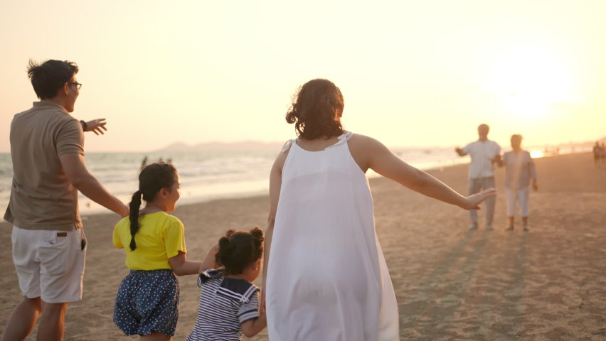 Happy big Asian family on beach holiday travel vacation. Multi-generation family enjoy outdoor lifestyle walking together on the beach at summer sunset. Grandparent embracing grandchild girl with love