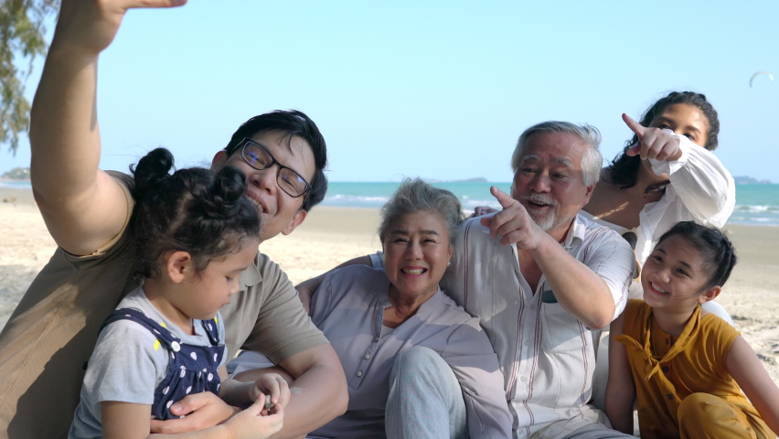 Happy Multi-generation Asian family on summer holiday vacation. Grandparents, parents with two child girl kid enjoy and having fun using smartphone selfie or talking video call together on the beach. Royalty-Free Stock Footage #1069525369