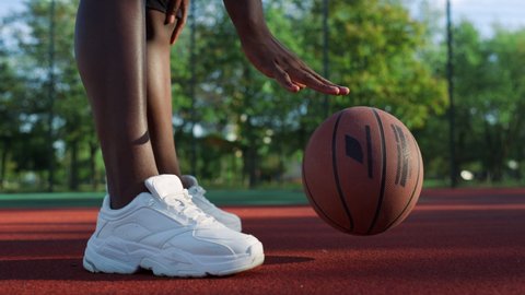 Unknown afro street basketball player training alone. Closeup hands bouncing basketball ball against background of legs in slow motion. Unrecognizable african guy practicing basketball exercise. 
