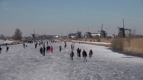 KINDERDIJK, NETHERLANDS – 13 FEBRUARY 2021: People ice skate on frozen canals with beautiful historic windmills as backdrop. A welcome break from continuiing lockdown measures in the Netherlands.
