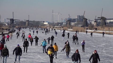 KINDERDIJK, NETHERLANDS – 13 FEBRUARY 2021: People ice skate on frozen canals past windmills, enjoying a traditional Dutch sport (a welcome break from Covid-19 lockdown).