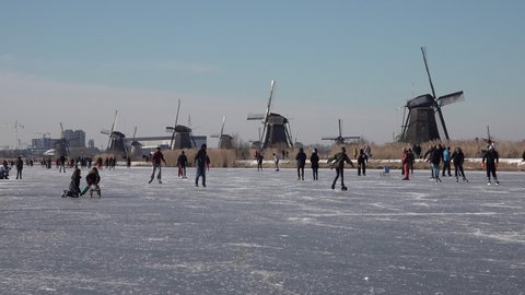 KINDERDIJK, NETHERLANDS – 13 FEBRUARY 2021: Classic Dutch Winter landscape, with people having fun and ice skating in typical Dutch landscape of windmills. 