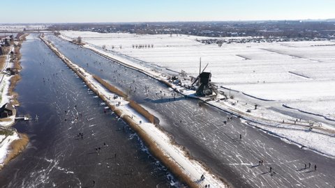 Classic Dutch Winter landscape seen from above. Drone flight of people having fun and ice skating in typical Dutch landscape of windmills in small village Kinderdijk.