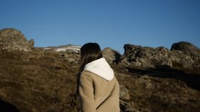 A girl in a beige jacket and white hooded jacket runs up walking high in the mountains. Travel video. High quality FullHD footage