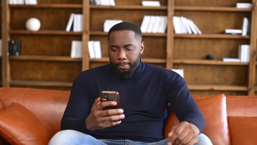 Shocked African-American man holding a smartphone, feel astonishment with a bad news, fired from work, irritated guy looks at phone screen and does not understand what happened Royalty-Free Stock Footage #1069542502