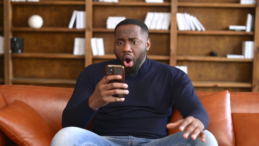 Shocked African-American man holding a smartphone, feel astonishment with a bad news, fired from work, irritated guy looks at phone screen and does not understand what happened | Shutterstock HD Video #1069542502