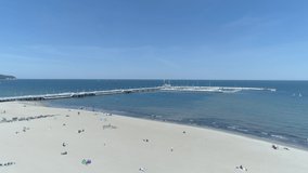 Pier in Sopot, Poland, visible on the video from the drone. In the foreground a sandy beach with people relaxing. In the background, the Baltic Sea and the famous pier on it.