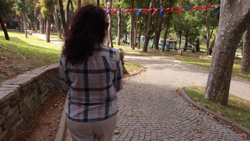 A woman in a protective mask walks and rests in a green park on a sunny summer day