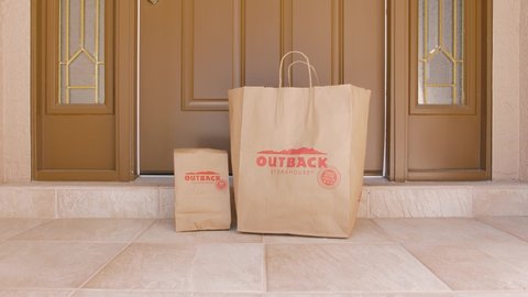 NORTH PORT, FLORIDA - MARCH 24, 2021: Man retrieving Outback Steakhouse delivery take out food order delivered to home doorstep.