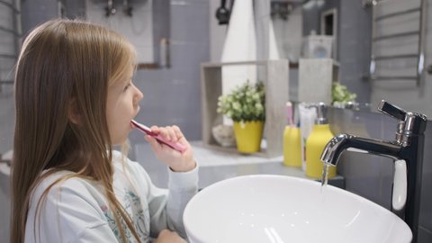 A little girl brushes her teeth. Early morning.