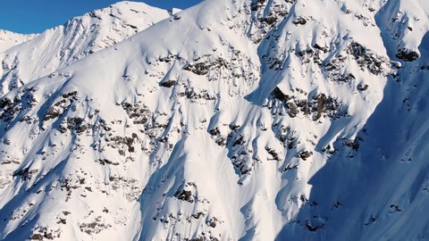 Aerial view of a delightful mountain range covered with snow and glaciers and mountain peaks with avalanche-prone couloirs against a blue sky on a clear sunny day in the high mountains