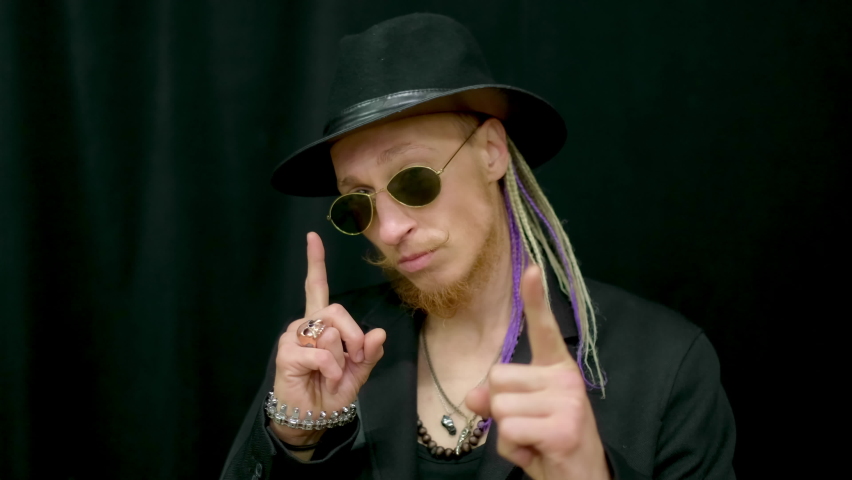 Hipster dreadlocks hairstyle looking at camera. Portrait hat bearded rocker man. Punk sunglasses gesturing hands. Look fashion hipster. Portrait face people rocker in glasses. Magic motion arm gesture
