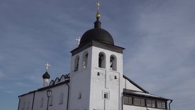Birds fly past an Orthodox old church with white walls and a golden cross against the blue sky in winter. snow on the roof. High quality 4k footage