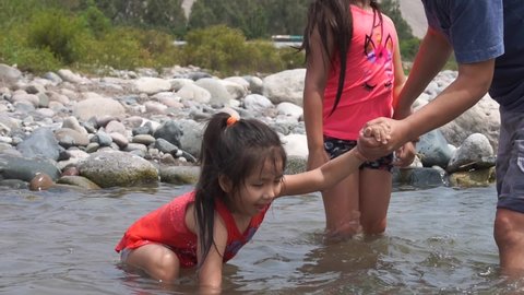 slow motion of a dad holding his daughter to play with the water in a stream near the river on a family vacation trip during the day