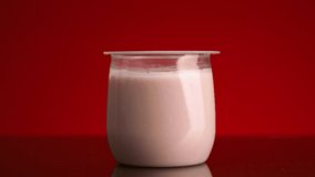 Close-up of yogurt in glass cup on red background. Stock footage. Hand with spoon takes yogurt from glass on isolated background. Sample of delicious yogurt in clear glass