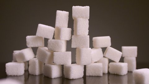 Sugar cubes on isolated background. Stock footage. Tower of sugar cubes collapses on isolated background. Sweets in large quantities are harmful to health. Sugar and sweets are 21st century addiction