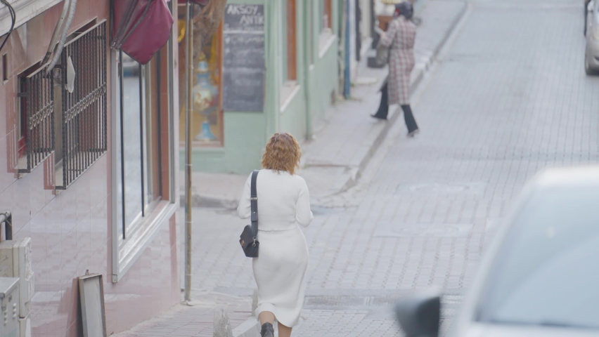 Beautiful woman photographs streets of town. Action. Attractive woman in white dress takes pictures of busy town on camera
