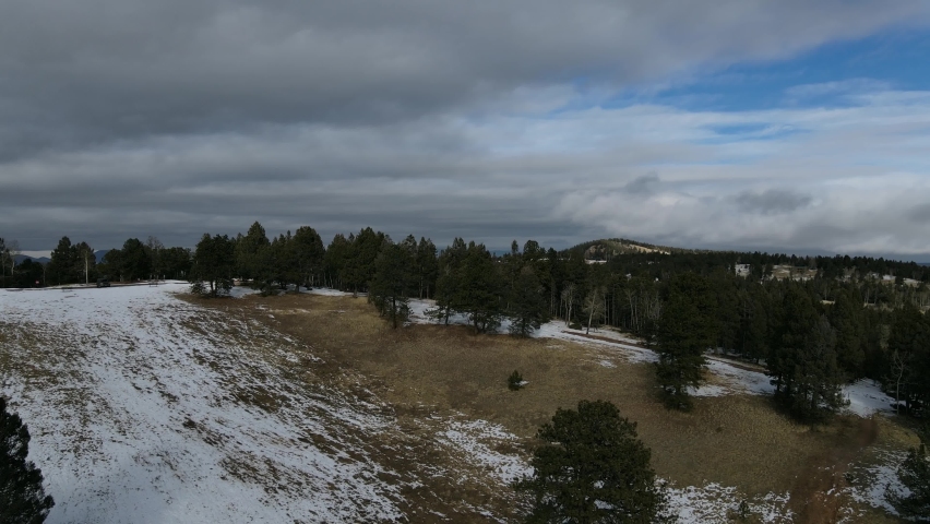 Aerial view panning right shot, Scenic view Pine Tree Forest on the snow covered mountain hills of Pikes Peak, Colorado Springs, Mountain range and cloudy blue sky in the background.