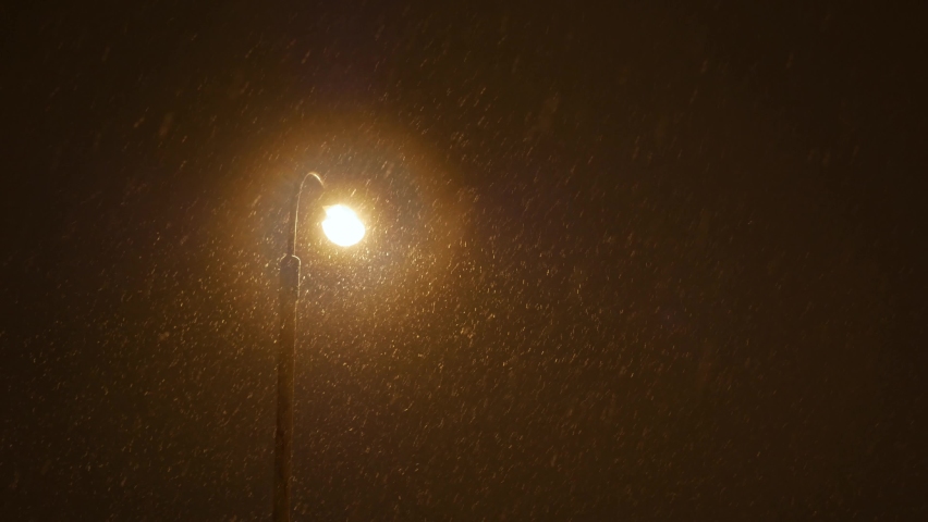 Snow falling in the yellow light of street lamp at night