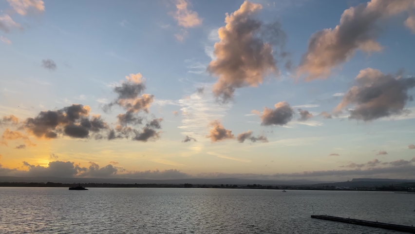 Dreamy sunrise with colorful clouds over calm rippled water, static shot