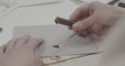 A person letting sealing wax fall on the edge of a letter in order to seal it. Handheld shot.