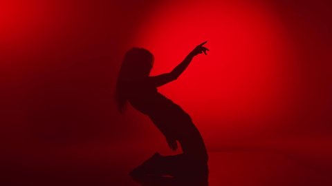 Sensual feminine performing stretching strip plastic dance at darkness night party stage slow motion. Silhouette of professional dancer lady dancing isolated at red studio. Wide shot on RED camera