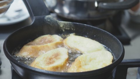 Pouring sugar with cinnamon topping over torrijas (Spanish french toast). Close up of torrijas soak bread being fried on hot oil in a pan. Typical food for easter holidays