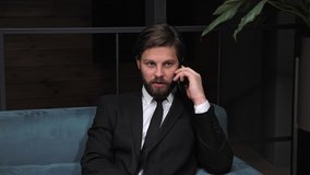 Stylish businessman with a beard in a classic suit is negotiating with partners by phone in a modern office building Business. Social Networking. People. Apps.