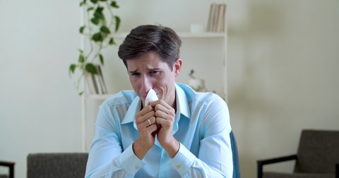 Adult upset businessman feeling stress, guy crying sobbing, wiping his nose with napkin handkerchief, close up people grief emotions. Office worker male comically funny suffering sitting at home