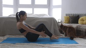 Young woman blogger shoots video doing Yoga exercise with phone while Maine Coon cat is sitting side by side at home. Sport and fitness. Training, workout and wellness concept. During Quarantine.