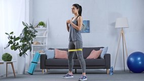 Sportswoman doing squats with resistance band while training at home