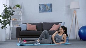 Smiling sportswoman training on fitness mat in living room