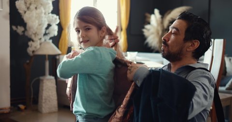 Dad helps his daughter put on a jacket, the parent prepares the child to go to school