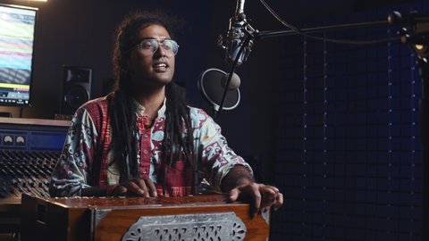 Music production studio. Creative world. Hindi man playing harmonium in the sound studio. A long hair brunette male person in a traditional shirt plays meditation music.