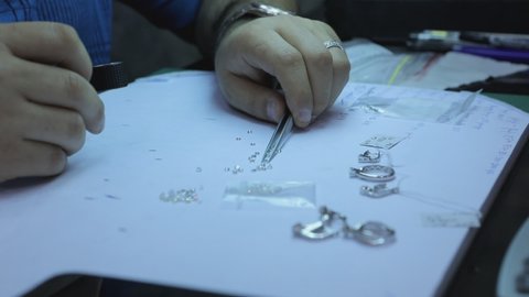 A goldsmith in jewelry checks the quality of luxury brilliant diamonds . The diamonds of high caliber shine the light and pure . Many expensive and small crystals lay on table on diamond shop . 