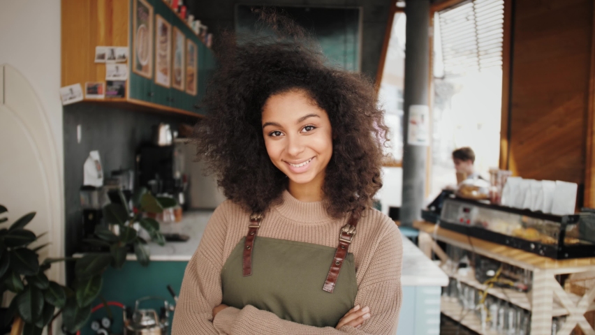 African American woman small business owner, generation z female with Afro hair looks at camera stands in cafe interior. Smiling mixed race latin young woman portrait. Work for international students | Shutterstock HD Video #1069599631