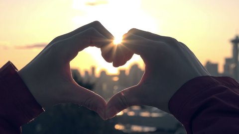 Heart shaped hand gesture with Seattle and bright morning sun behind