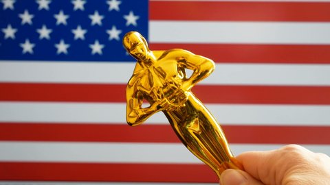Hollywood Golden Oscar Academy award statue on american flag background with copy space. Success and victory concept.