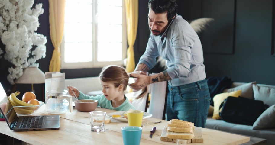 Business dad make  hairstyle to  his daughter. Businessman is preparing his daughter for school and talking on the phone. Family morning over breakfast. Getting ready for work and school Royalty-Free Stock Footage #1069600987